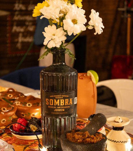 Flower vase made out of liquor bottle on a table with traditional Mexican food.