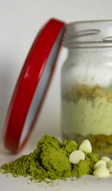 Green matcha desert on the back in a glass jar, with matcha powder and white chocolate chips in front focus.